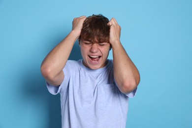 Photo of Teenage boy suffering from panic attack on light blue background