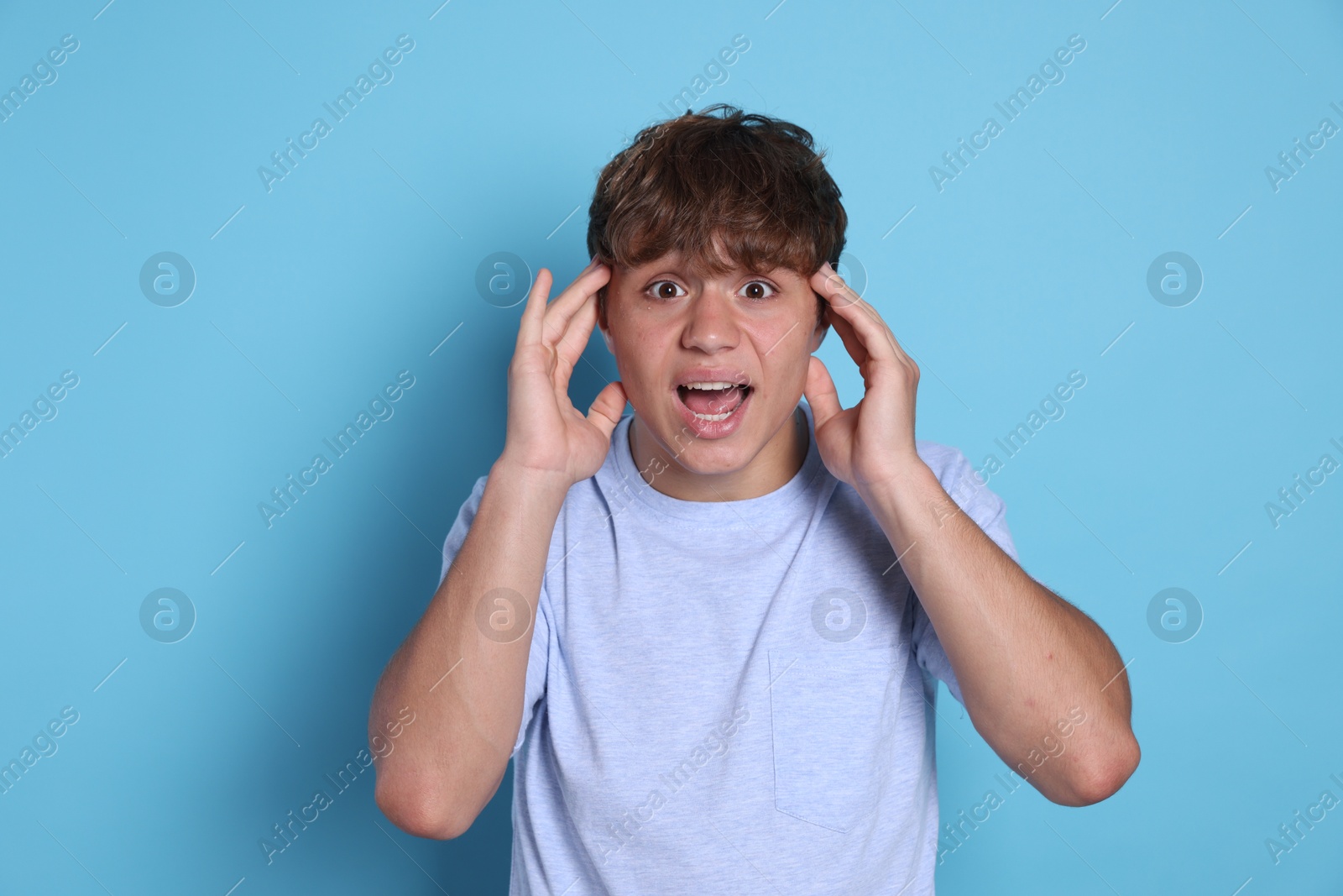 Photo of Teenage boy suffering from panic attack on light blue background