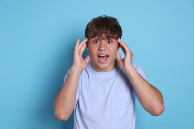 Photo of Teenage boy suffering from panic attack on light blue background