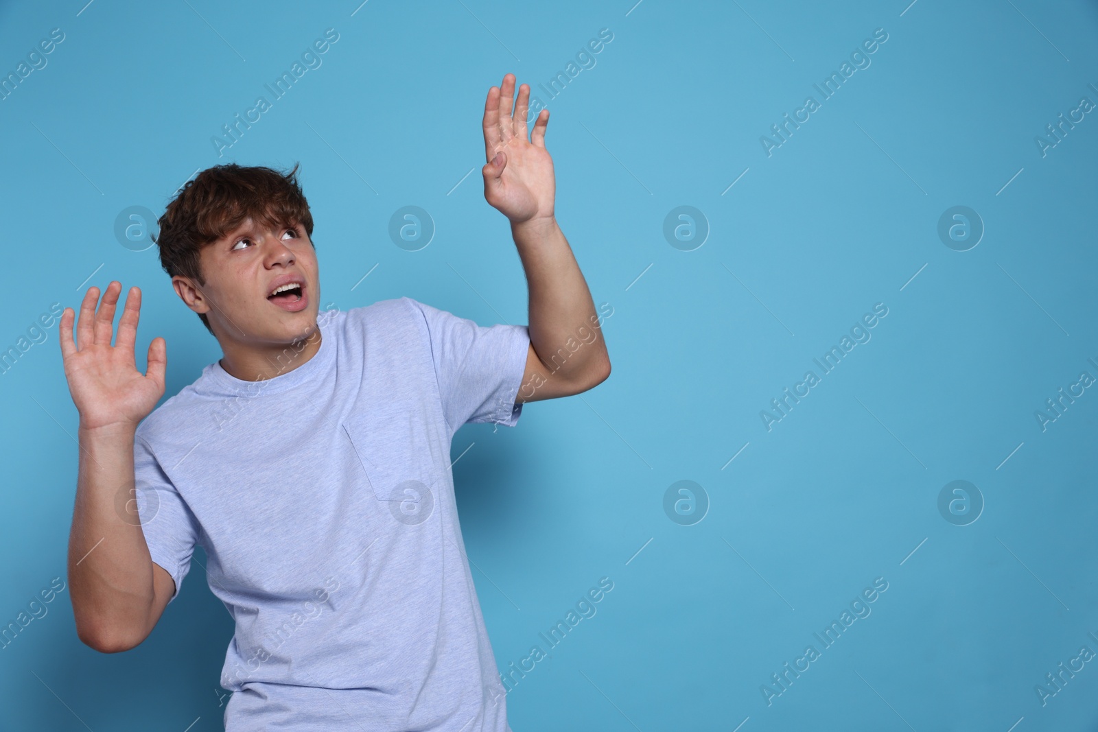 Photo of Teenage boy suffering from panic attack on light blue background. Space for text