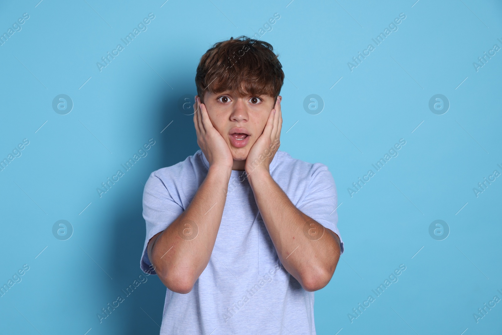 Photo of Teenage boy suffering from panic attack on light blue background