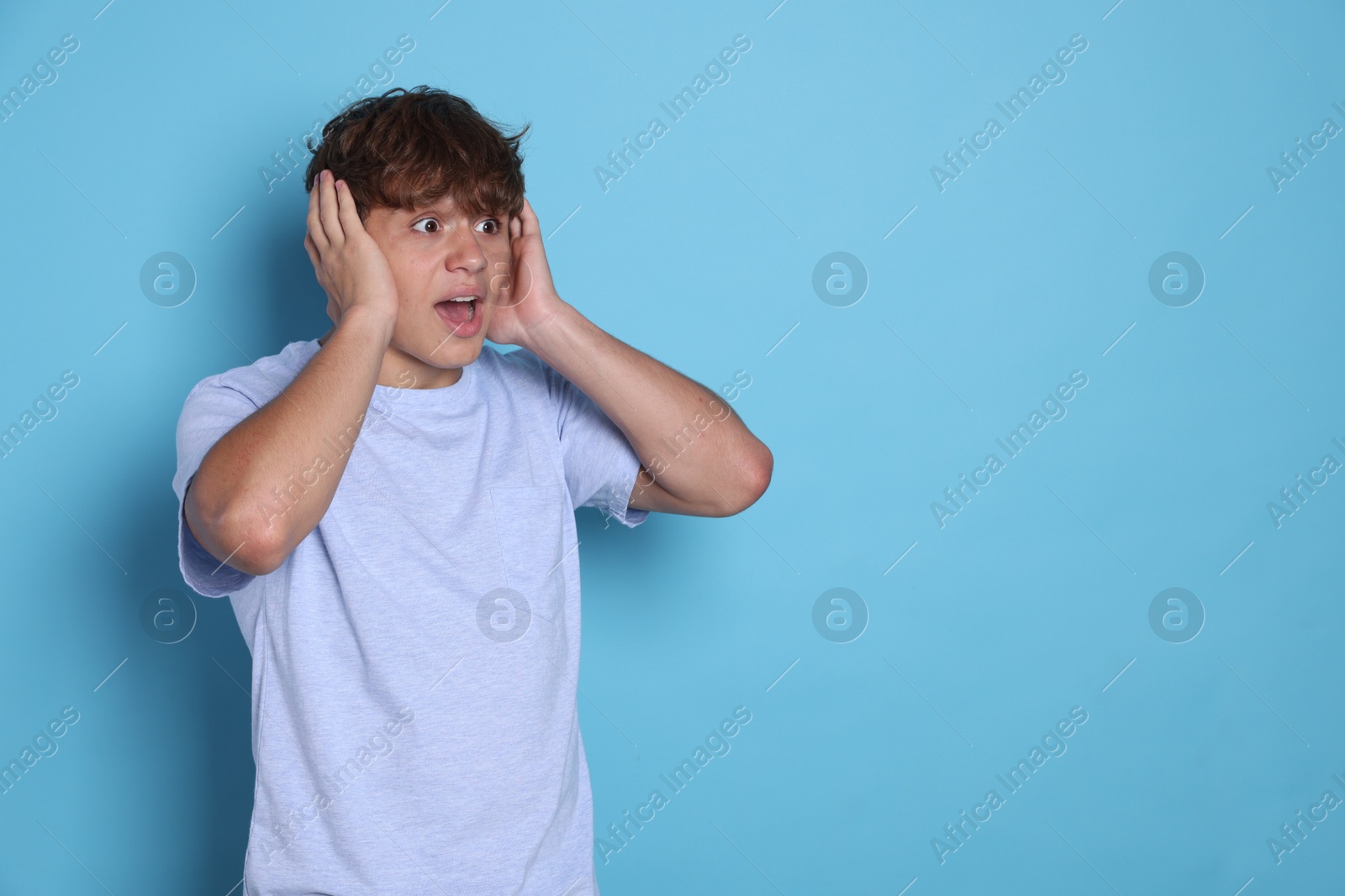 Photo of Teenage boy suffering from panic attack on light blue background. Space for text