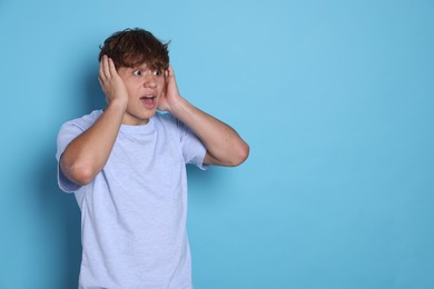 Photo of Teenage boy suffering from panic attack on light blue background. Space for text
