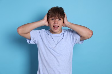 Photo of Teenage boy suffering from panic attack on light blue background