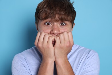 Photo of Teenage boy suffering from panic attack on light blue background