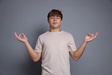 Photo of Teenage boy meditating on grey background. Way to stop panic attack