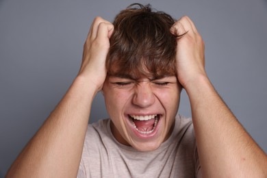 Photo of Teenage boy suffering from panic attack on grey background