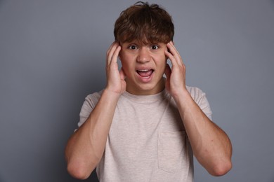 Photo of Teenage boy suffering from panic attack on grey background