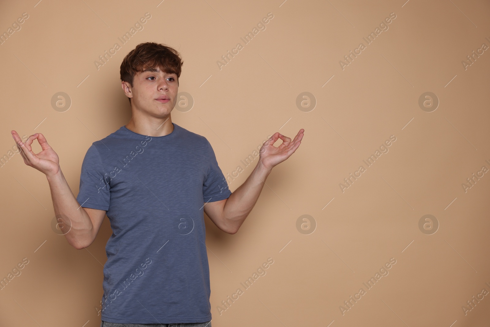 Teenage boy meditating on beige background, space for text. Way to stop panic attack Photo of Teenage boy meditating on beige background, space for text. Way to stop panic attack