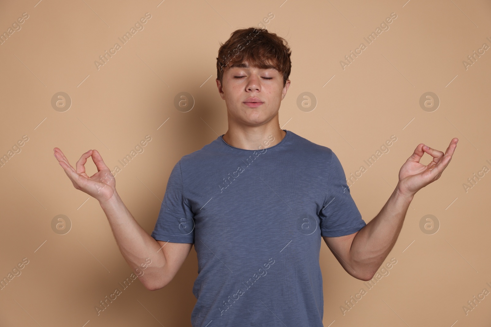 Photo of Teenage boy meditating on beige background. Way to stop panic attack