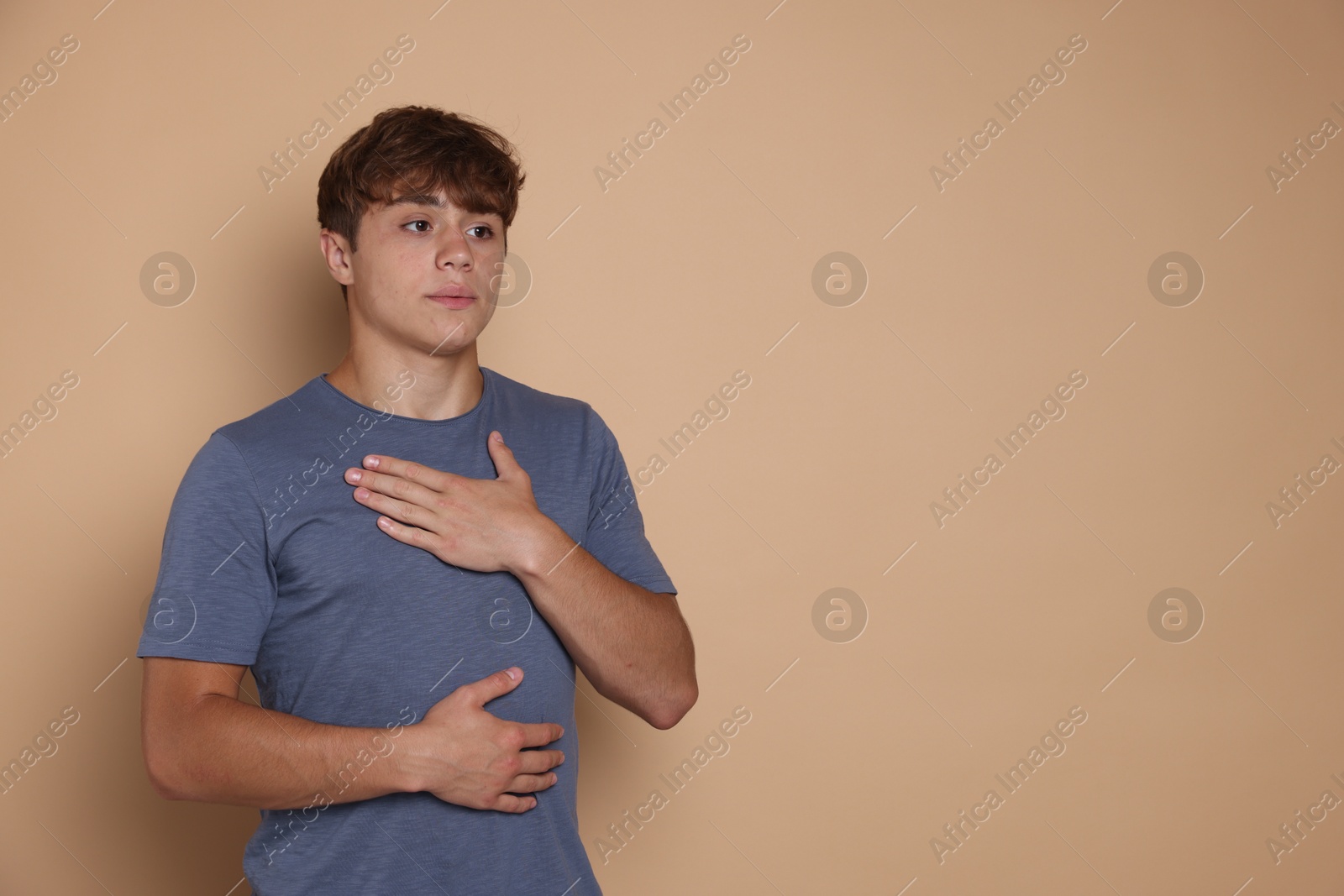 Photo of Teenage boy deep breathing on beige background, space for text. Way to stop panic attack