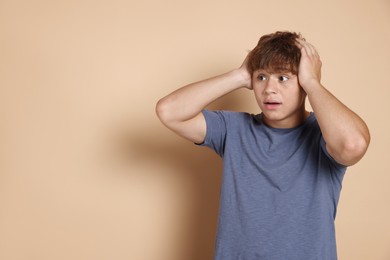 Photo of Teenage boy suffering from panic attack on beige background. Space for text