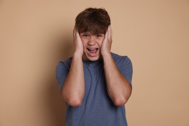 Photo of Teenage boy suffering from panic attack on beige background