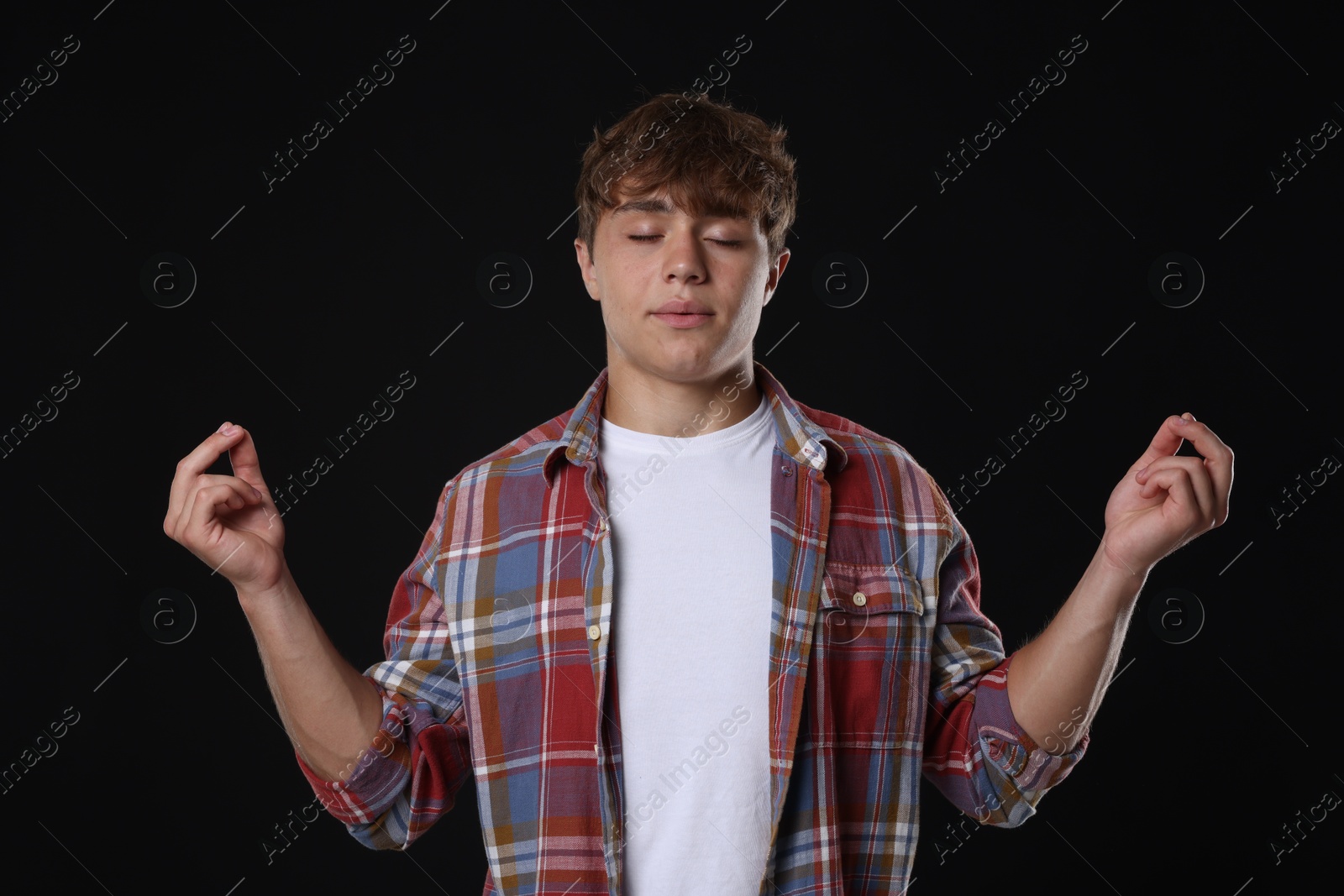 Photo of Teenage boy meditating on black background. Way to stop panic attack