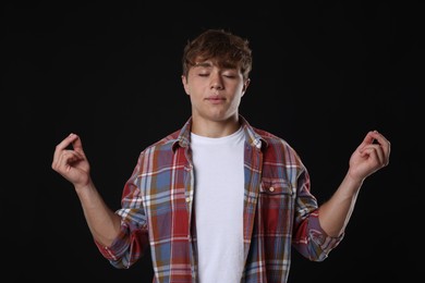 Photo of Teenage boy meditating on black background. Way to stop panic attack