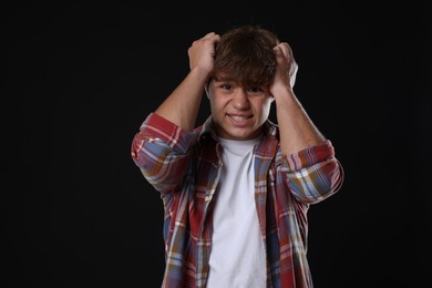 Photo of Teenage boy suffering from panic attack on black background
