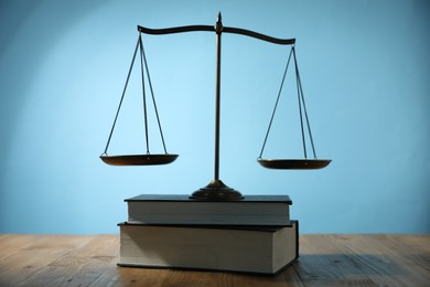 Photo of Scales of justice and books on wooden table against light blue background