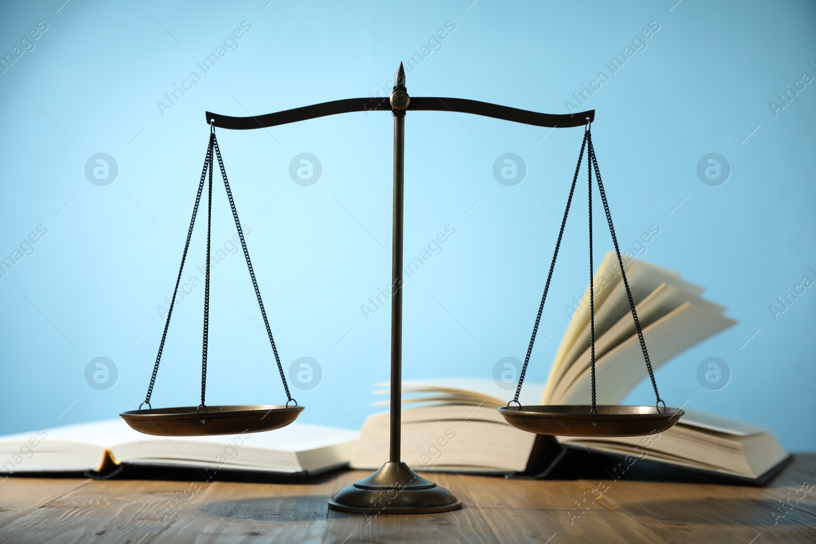 Photo of Scales of justice and books on wooden table against light blue background