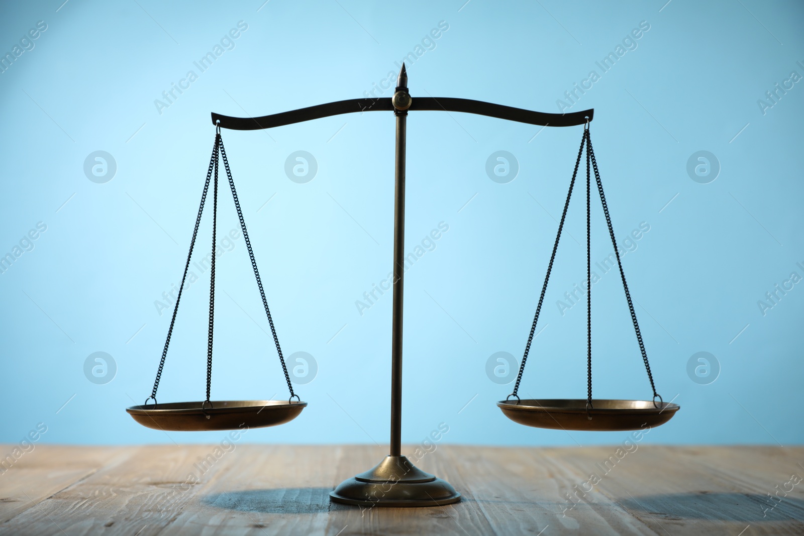 Photo of Scales of justice on wooden table against light blue background
