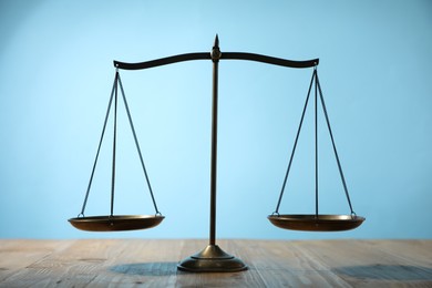Photo of Scales of justice on wooden table against light blue background