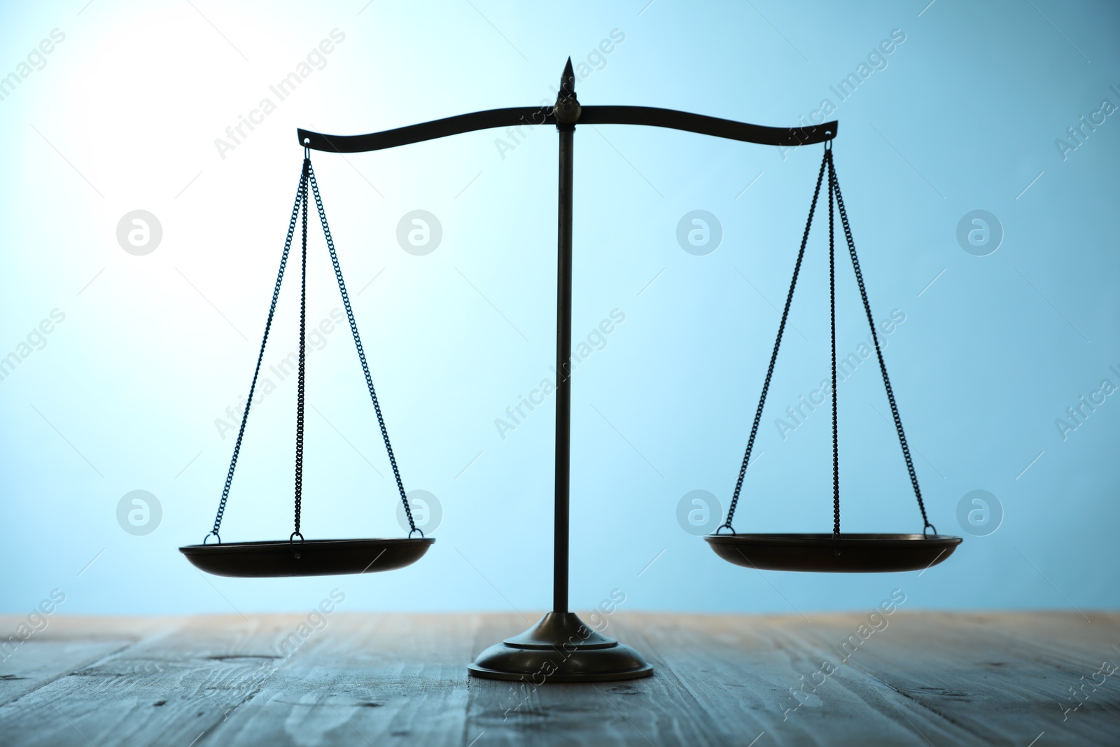Photo of Scales of justice on wooden table against light blue background