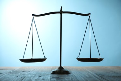 Photo of Scales of justice on wooden table against light blue background