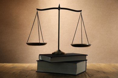 Photo of Scales of justice and books on wooden table against beige background