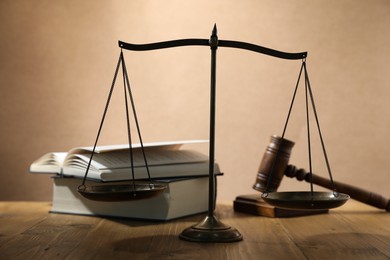 Photo of Scales of justice, gavel and books on wooden table against beige background, selective focus