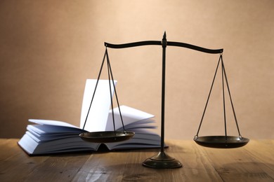Photo of Scales of justice and book on wooden table against beige background, selective focus