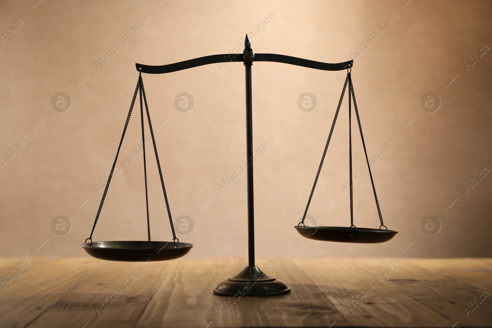 Photo of Scales of justice on wooden table against beige background