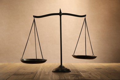 Photo of Scales of justice on wooden table against beige background