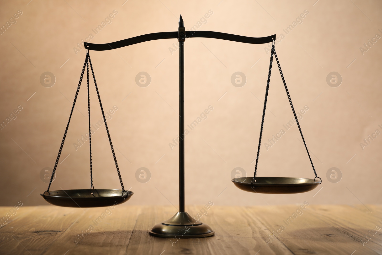 Photo of Scales of justice on wooden table against beige background
