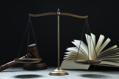 Photo of Scales of justice, gavel and book on grey table against black background, selective focus
