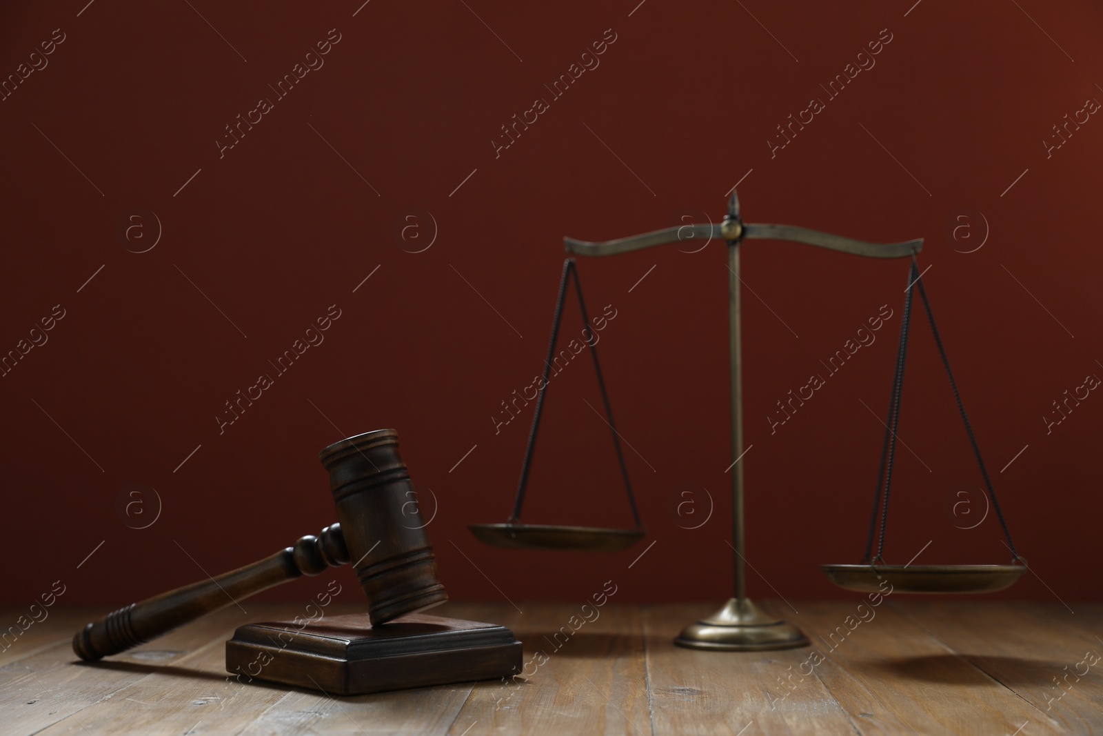 Photo of Gavel and scales of justice on wooden table against maroon background, selective focus