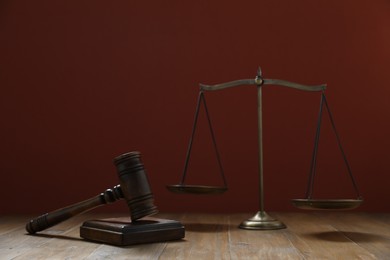 Photo of Gavel and scales of justice on wooden table against maroon background, selective focus