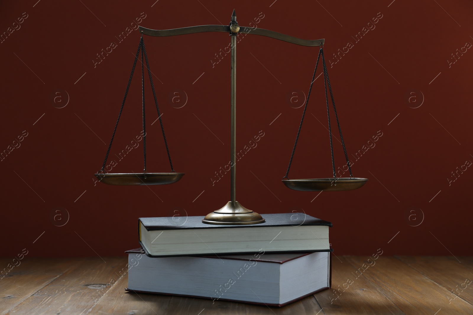 Photo of Scales of justice and books on wooden table against maroon background