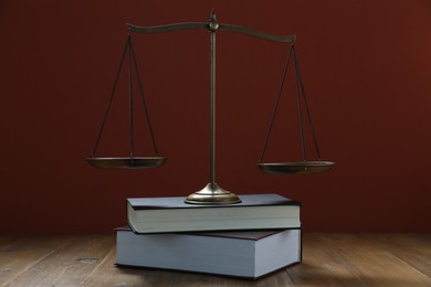 Photo of Scales of justice and books on wooden table against maroon background