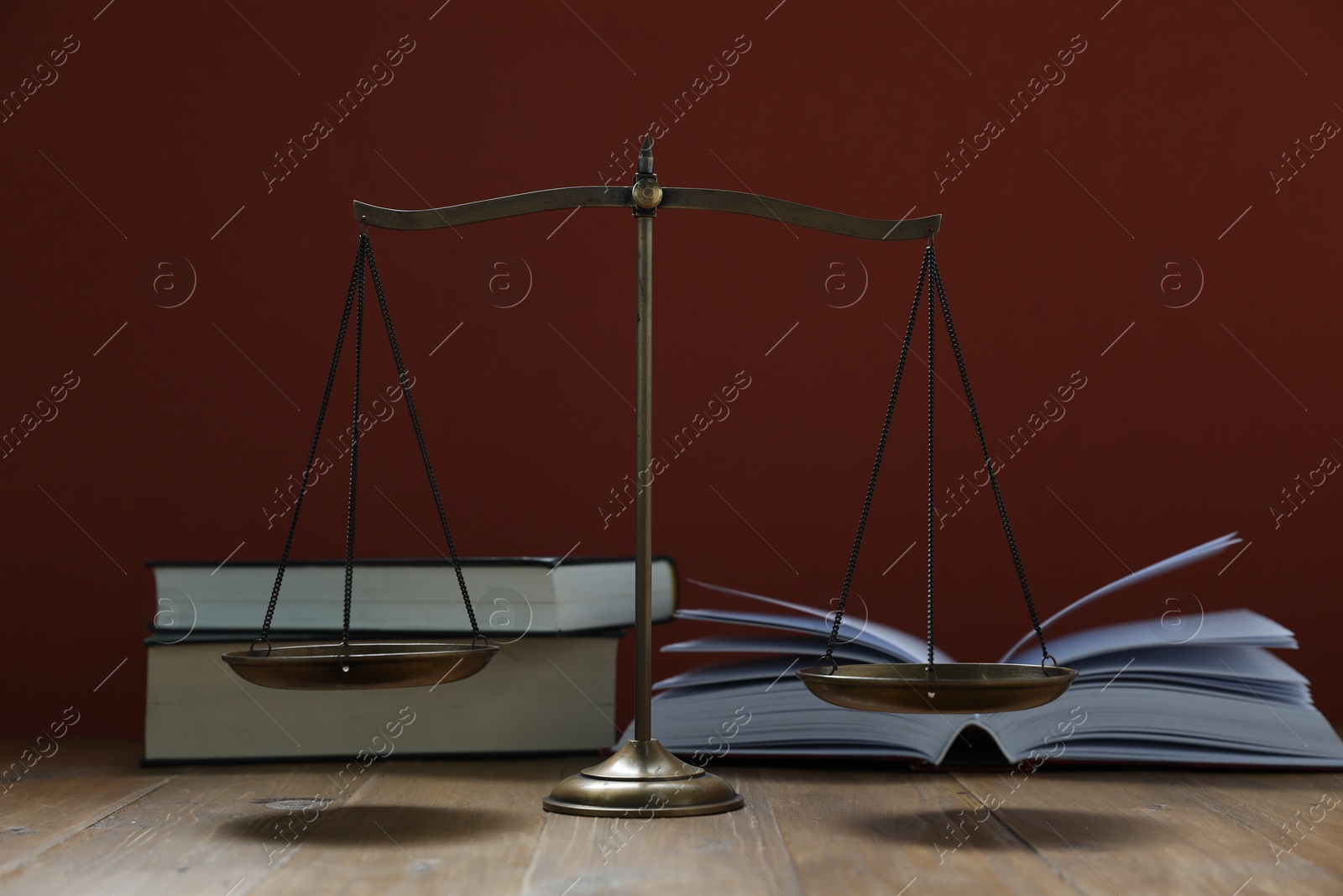 Scales of justice and books on wooden table against maroon background Photo of Scales of justice and books on wooden table against maroon background