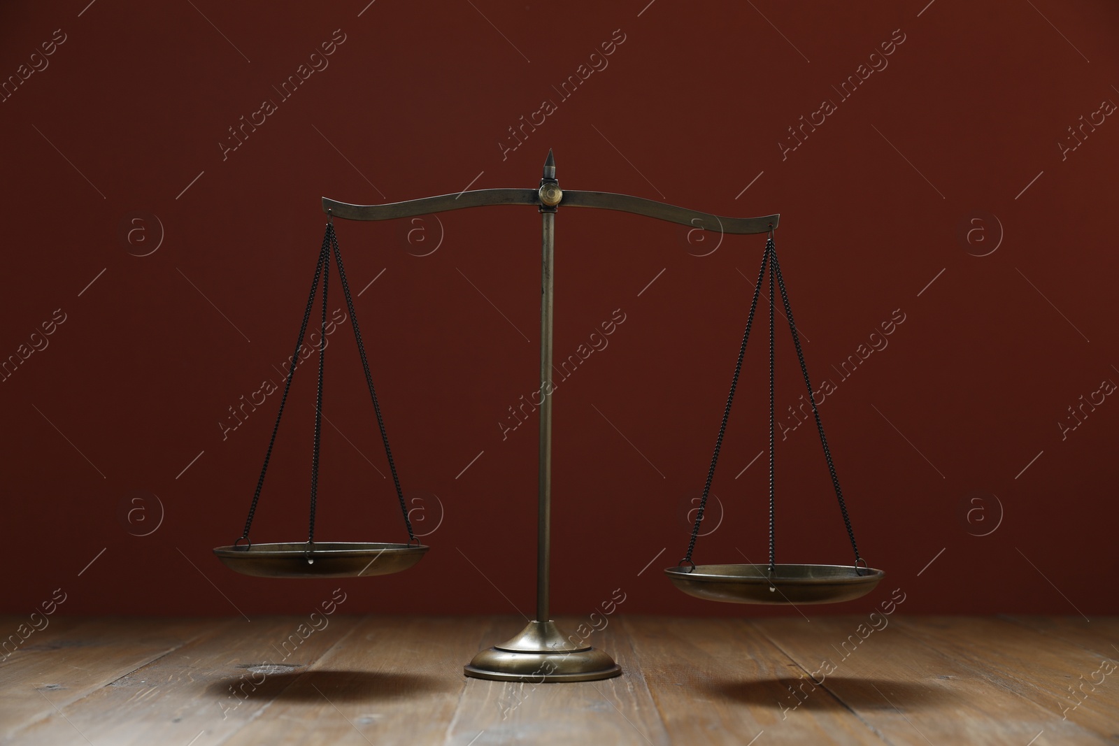 Scales of justice on wooden table against maroon background Photo of Scales of justice on wooden table against maroon background