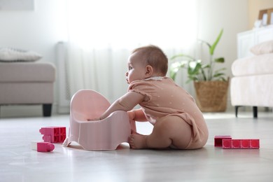 Photo of Cute little baby sitting near potty and toys on floor at home