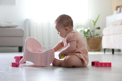 Photo of Cute little baby sitting near potty and toys on floor at home