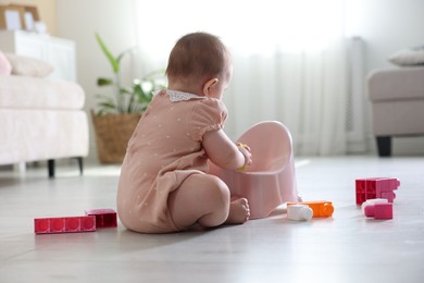 Photo of Cute little baby sitting near potty and toys on floor at home
