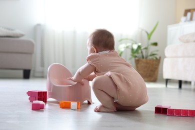 Photo of Cute little baby with potty and toys on floor at home
