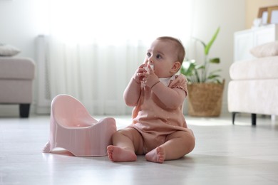 Photo of Cute little baby with toy sitting near potty on floor at home