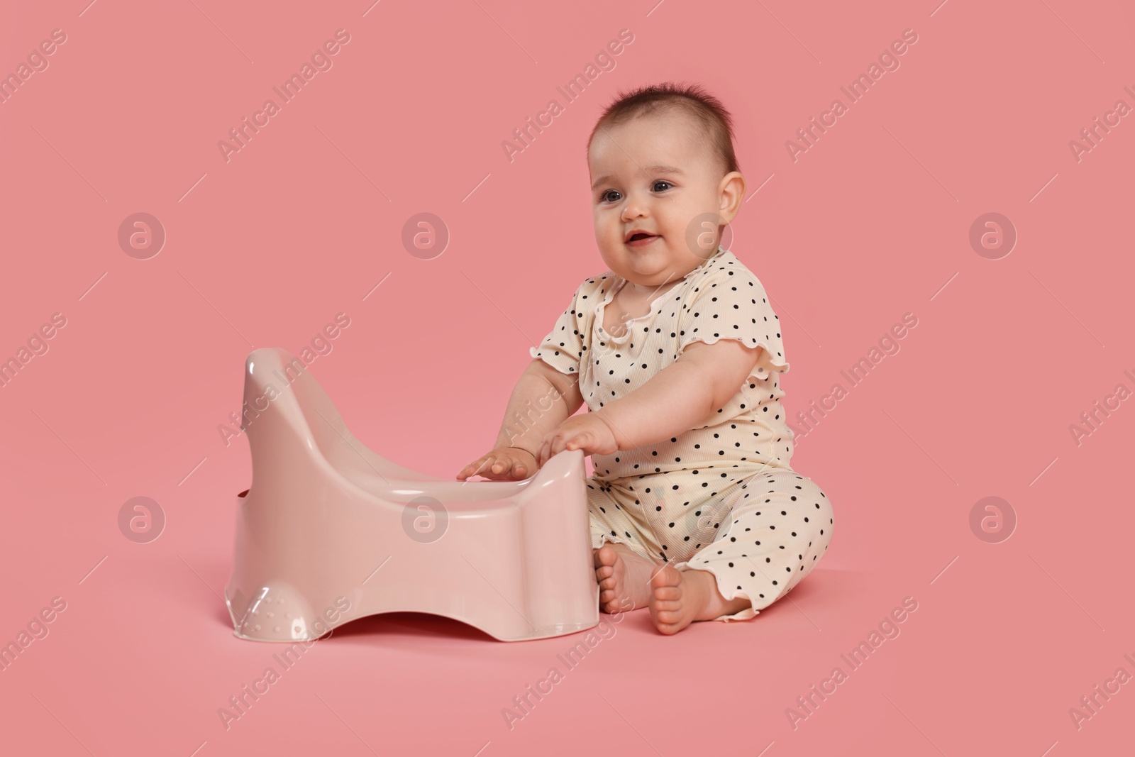 Photo of Cute little baby sitting near potty on pink background