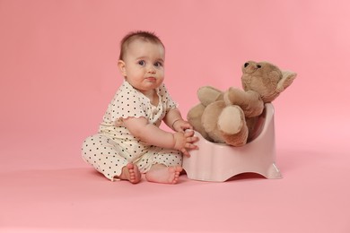 Photo of Cute little baby sitting near potty with toy bear on pink background