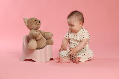 Photo of Cute little baby sitting near potty with toy bear on pink background