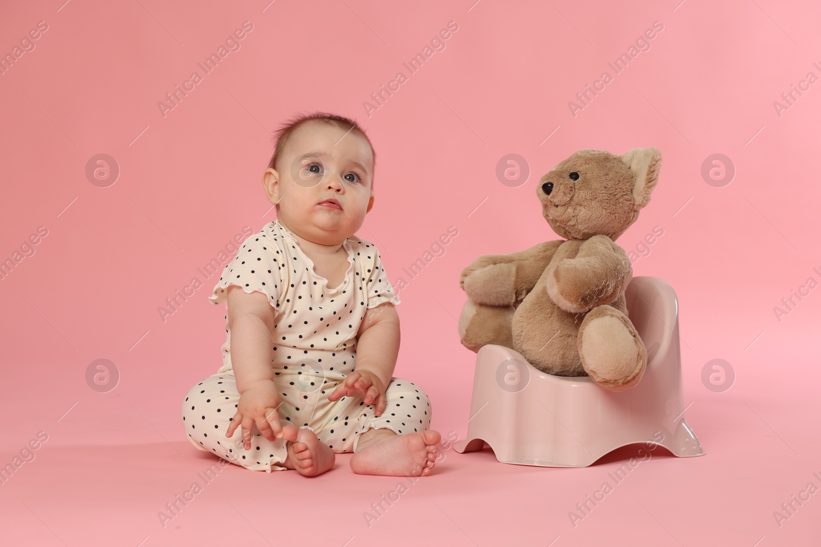 Cute little baby sitting near potty with toy bear on pink background Photo of Cute little baby sitting near potty with toy bear on pink background