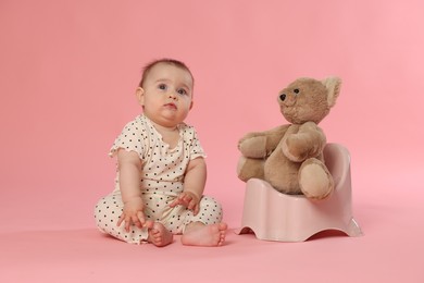 Photo of Cute little baby sitting near potty with toy bear on pink background
