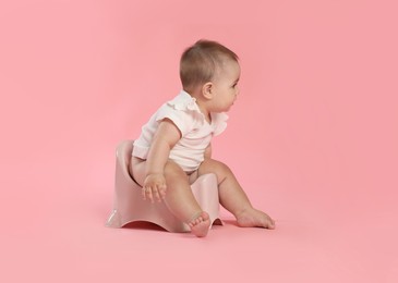 Photo of Cute little baby sitting on potty against pink background